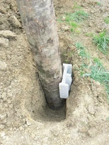 Le poteau est calé avec des matériaux durs : résidus de parpaings, gros cailloux, etc. notamment sur le devant